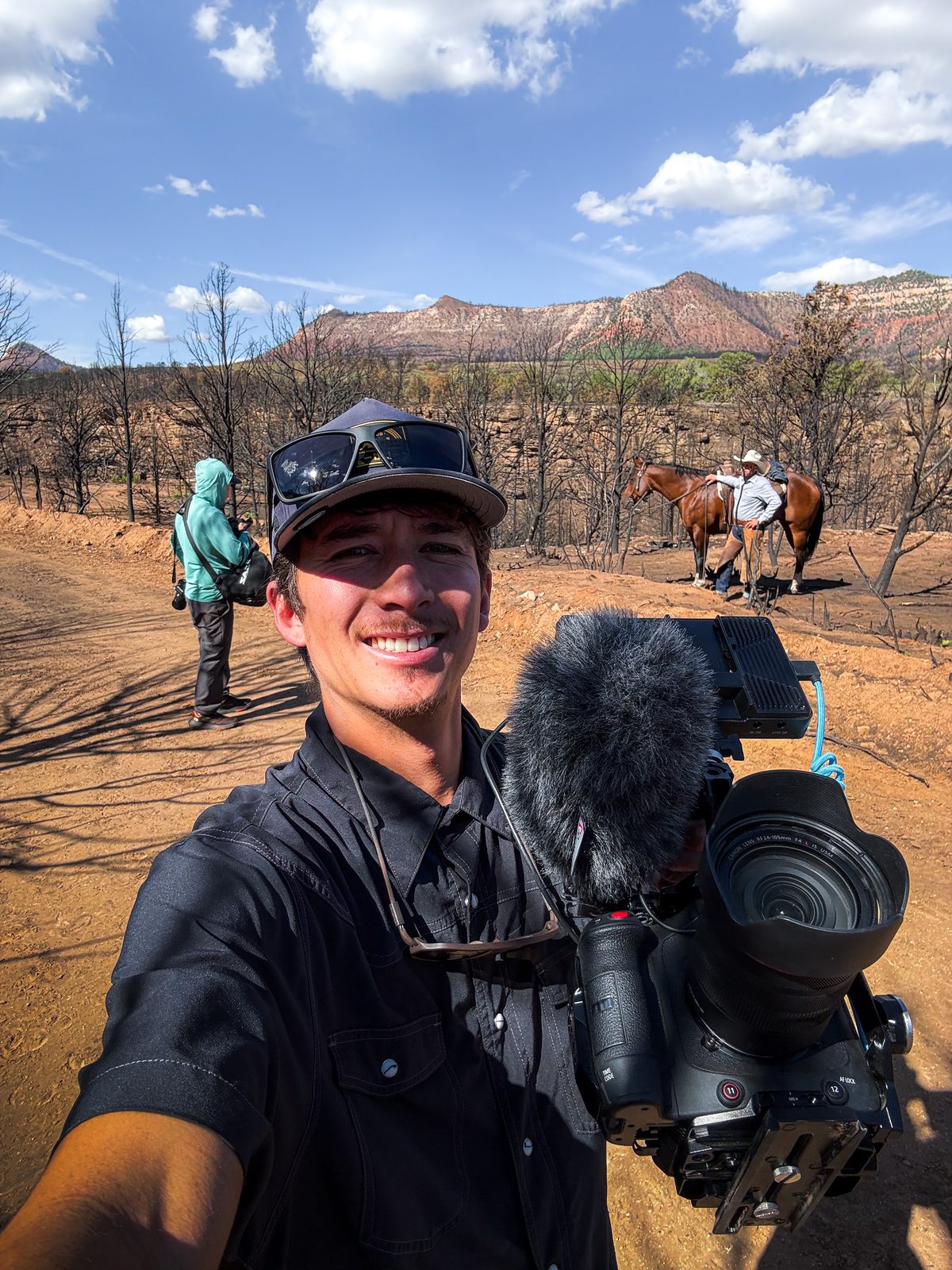 Kaulike Jansen with a Canon C80 in a burned forest, red-rock mountains and a horse behind